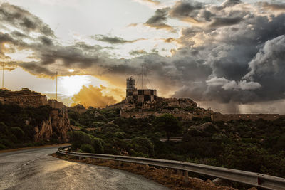 Road amidst buildings against sky during sunset