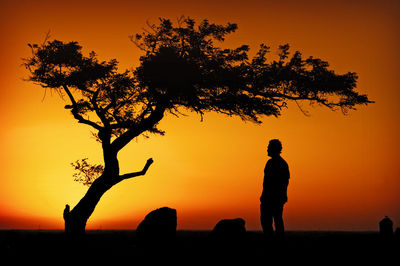 Silhouette man standing by tree against orange sky