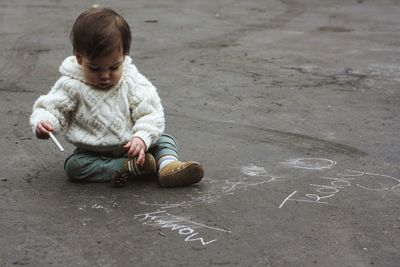 Baby boy sitting on asphalt with crayon