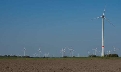 Wind turbines on field against clear blue sky