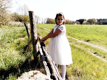 Girl standing by fence on land during sunny day