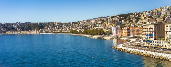 View of buildings by sea against clear blue sky