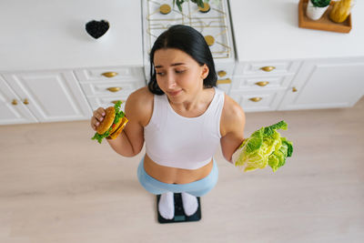 Young woman makes a choice between healthy and unhealthy food and stands on the scales person