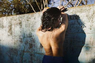 Rear view of shirtless woman standing against wall