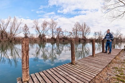 Rear view of man standing on jetty against lake