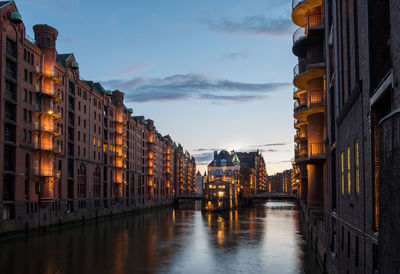 Canal amidst buildings in city against sky at dusk