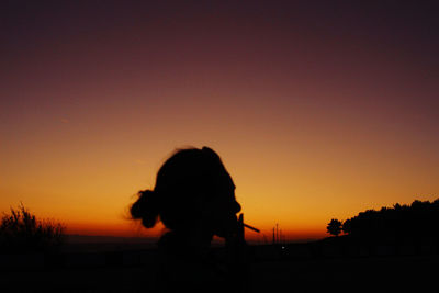 Silhouette woman standing against orange sky during sunset