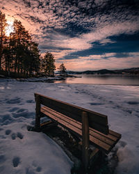 Bench on snow covered park during sunset