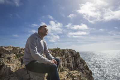 Man sitting on rock by sea against sky