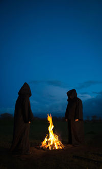 People sitting by bonfire against clear blue sky