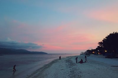 People on beach against sky during sunset