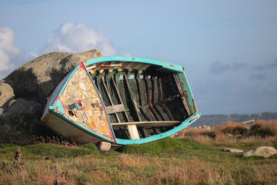 Abandoned boat on field against sky