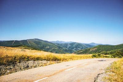 Road surrounded by vegetation against mountains and blue sky