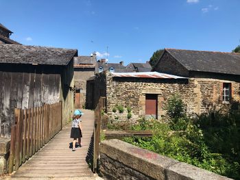 Rear view of man walking on footpath amidst buildings against sky