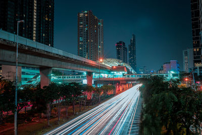 Light trails on street amidst buildings against sky at night