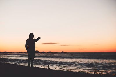 Silhouette of person standing by sea during sunset