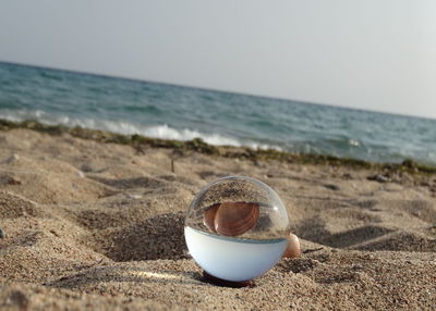 Crystal ball on sand at beach against sky