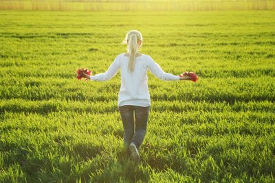 Rear view of woman holding flowers while walking on grassy field