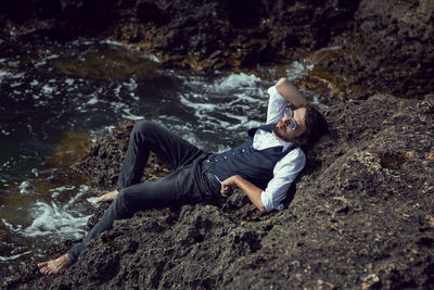 Man with a beard in dark clothes and a white shirt sits on the stone seashore in  crimea tarkhankut