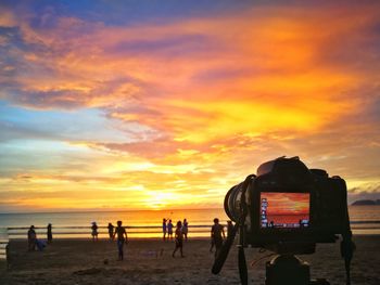 Silhouette people on beach against orange sky