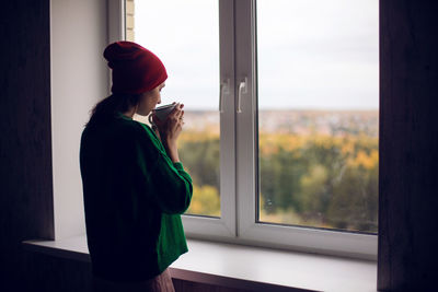 Woman in a green sweater holds a metal mug of cocoa and marshmallows