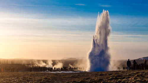 People standing by geyser on field against sky