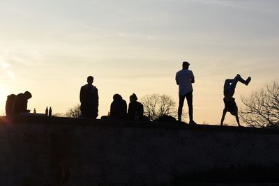 Friends enjoying on field against sky during sunset