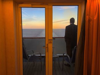 Rear view of man sailing on ship seen from closed glass door during sunset