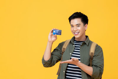Portrait of smiling man holding camera while standing against yellow background