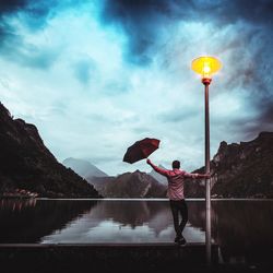 Rear view of woman with balloons standing by lake against sky