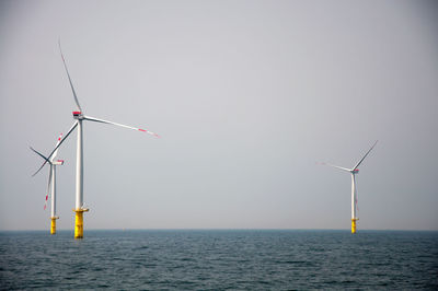 Wind turbines in sea against clear sky