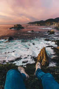 Low section of man on beach against sky during sunset