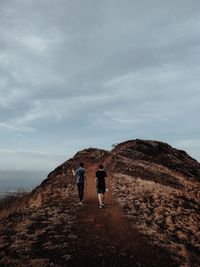 Rear view of man walking on mountain against sky