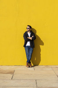 Young bearded man standing against a yellow wall with crossed arms