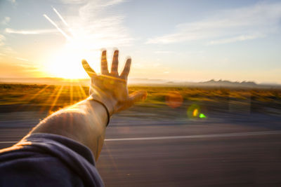 Hand in motion outside of car-window set against setting sun w/ mts