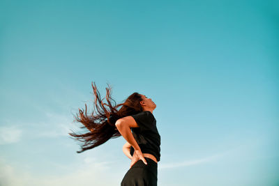Low angle view of woman with long hair standing against clear blue sky