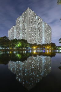 Illuminated buildings by river against sky at night