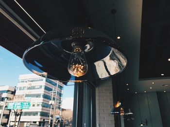 Low angle view of illuminated light bulb hanging on ceiling in building