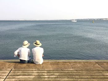 Rear view of couple sitting on sea shore against clear sky