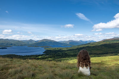 Rear view of girl sitting on field against sky