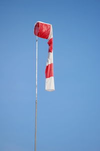 Low angle view of red and white windsock against clear blue sky