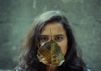 Close-up portrait of young woman covering face with leaf