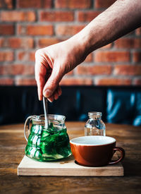 Cropped image of man stirring mint tea in jar on table