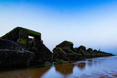 Rock formations by sea against clear blue sky