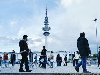 People walking in city against cloudy sky