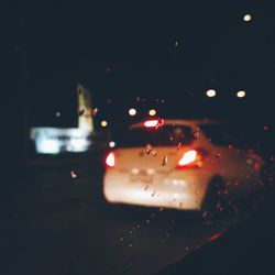 Cars on illuminated street seen through wet windshield