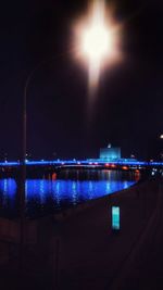 Illuminated city by river against sky at night