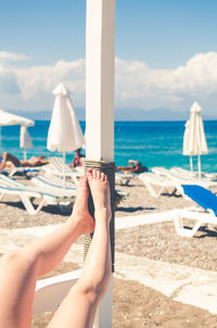 Low section of woman relaxing on beach against sky