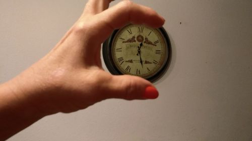 Close-up of hand holding clock against white wall