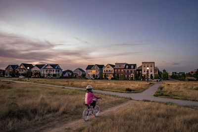 Rear view of man riding bicycle by building against sky